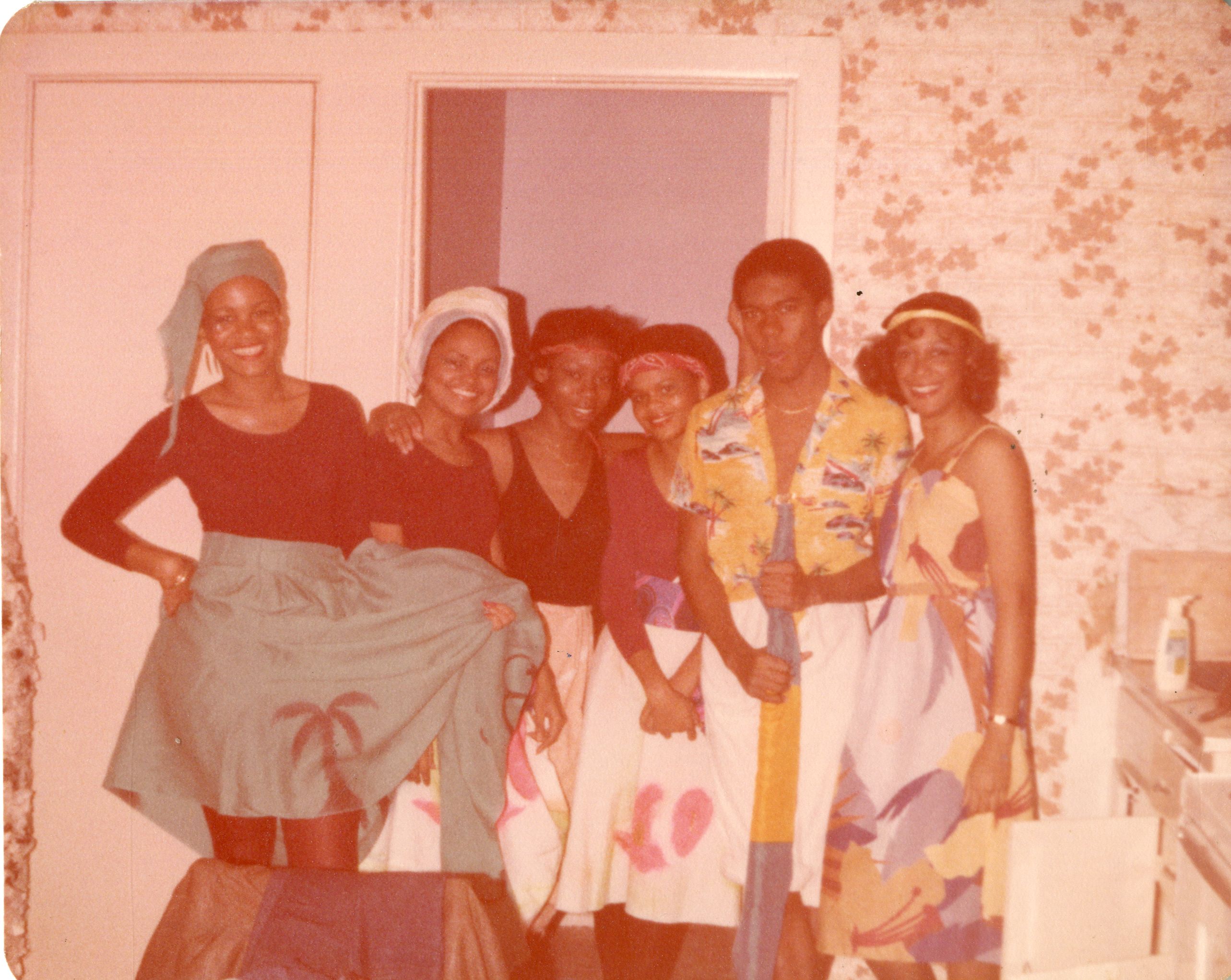 five Black females and 1 Black male posing in colorful Caribbean attire