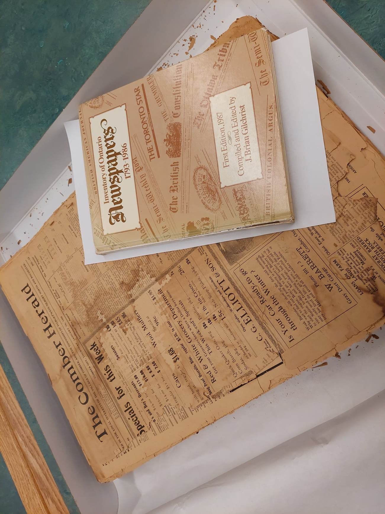 Image of a yellowed newspaper page from early 20th century, underneath a copy of a 1987 book index to historical newspapers.