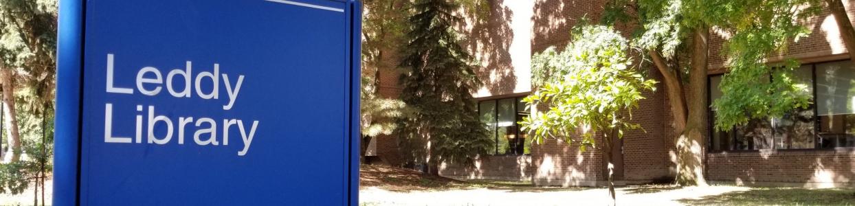 A picture of a blue sign in front of a building, with the words "Leddy Library"