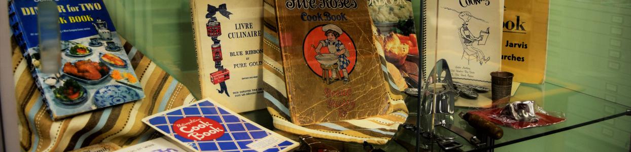 Historic cookbooks and cooking utensils in a glass display case