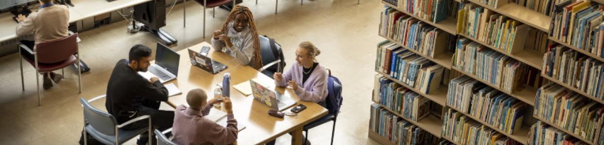 students sitting around a table near a bookshelf in the library 