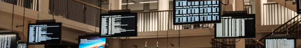 Photo of 6 screens hanging at various levels in a room with white text running across them.