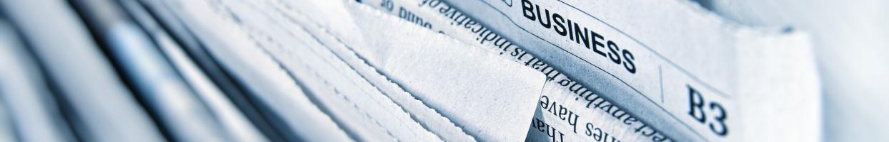 Photo of a bundle of newspapers with one poking above the rest. The top of that newspaper reads World Busines.