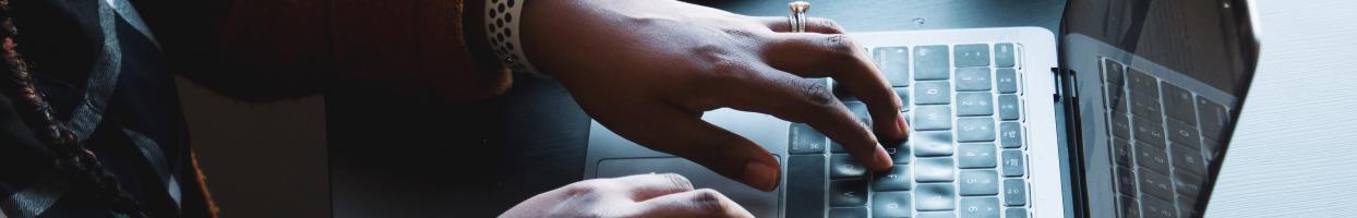 Photo of a Black woman's hand typing on a laptop keyboard. 