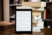 ebook reader displaying french text leaning against a stack of print books.